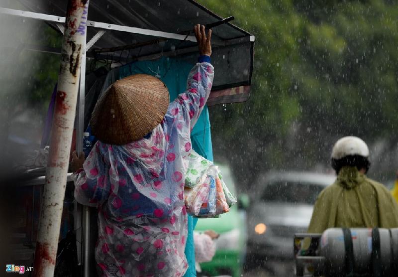 Một người phụ nữ bán áo mưa kéo mái che tránh mưa tạt vào quầy hàng.