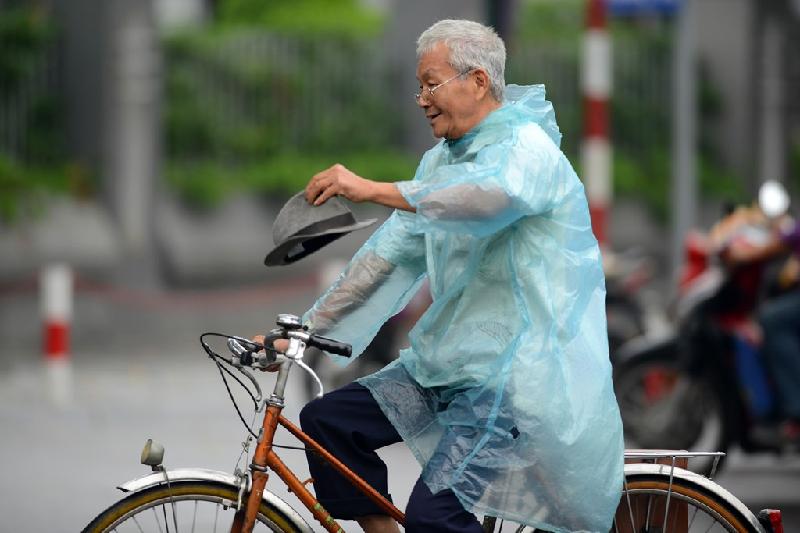 Cụ ông loay hoay với chiếc áo mưa mỏng và cái mũ phớt khi đạp xe ngoài phố.