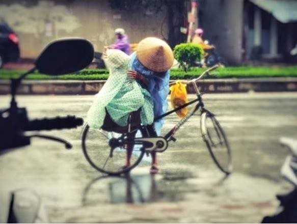 Ngày 15/8, diễn đàn hơn 200.000 thành viên chia sẻ bức ảnh trong cơn mưa tầm tã, người mẹ dừng xe đạp, mặc lại áo mưa cho con. Không ít dân mạng đã viết: Hình ảnh thật đẹp giữa đời thường. Ảnh: 