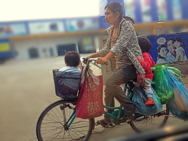 Người mẹ trên chiếc xe đạp cũ kỹ mang theo hai con nhỏ. Bức ảnh truyền tải thông điệp của tác giả: 
