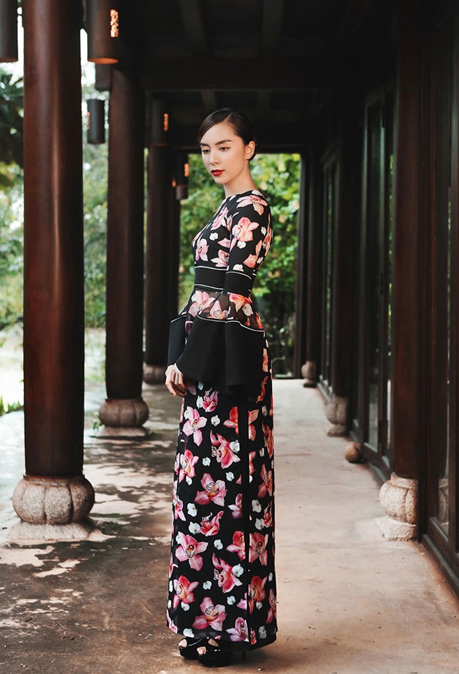 Áo dài của nhà thiết kế Adrian Anh Tuấn được thêm thắt nhiều chi tiết hiện đại như tay loe, lược cổ, họa tiết hoa nổi bật trên nền vải tối màu. Mảng cắt tại vòng eo tôn vóc dáng.