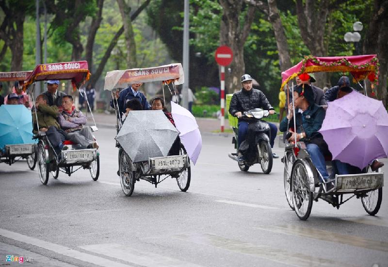 Bên hồ Gươm, nhóm du khách quốc tế đi dạo phố được tài xế xích lô chắn gió bằng những chiếc ô.