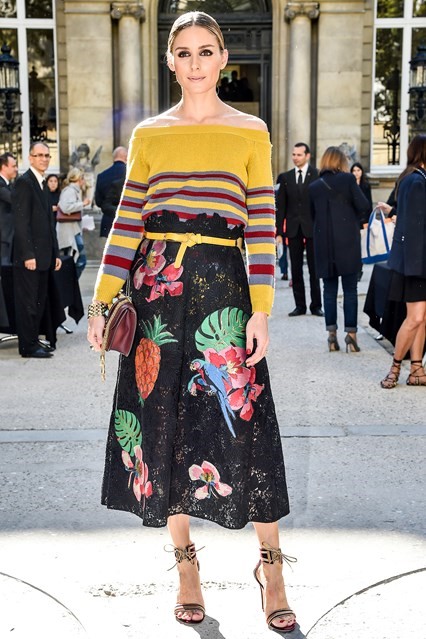 Olivia diện áo len trễ vai kẻ ngang trên nền tông vàng sáng phối cùng chân váy midi họa tiết thú vị khi tham dự tuần lễ thời trang Paris.