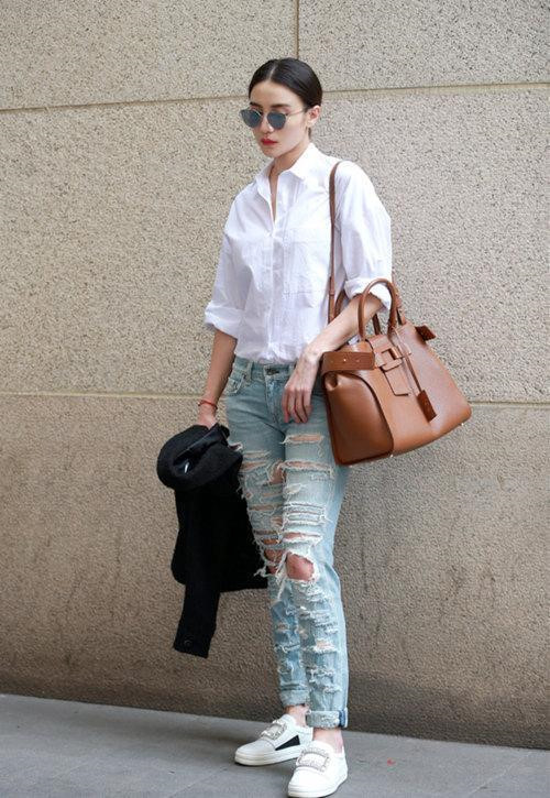 Nữ diễn viên Lý Phi Nhi đưa quần jeans xước rách “tả tơi” vào tổng thể chỉn chu với áo sơ mi và giày thể thao trắng. Phụ kiện kính mắt sành điệu và túi bản to tạo nét sành điệu.  