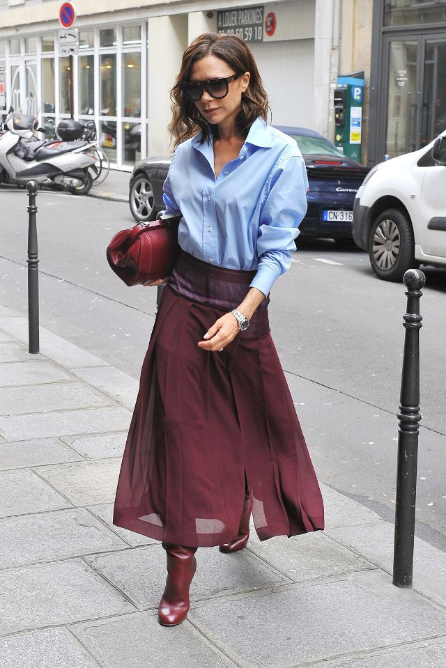 Victoria Beckham thanh lịch khi diện áo sơ mi xanh nhạt kết hợp với chân váy xuyên thấu xếp li màu đỏ rượu vang.