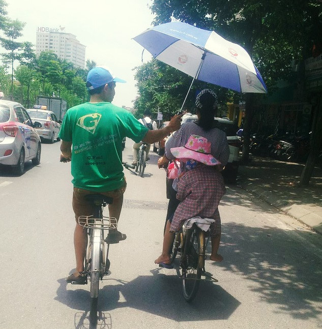 Hình ảnh người chồng dùng ô che cho vợ và con gái trên đường thu hút sự chú ý của cộng đồng mạng. Bức ảnh do anh Minh Nhân chụp trên đoạn đường Văn Cao, quận Ba Đình, Hà Nội. Ảnh: 
