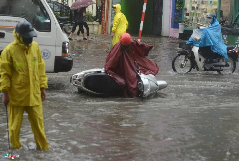 Do lóng ngóng trong chiếc áo mưa tránh đoạn nước ngập sâu và ôtô bên cạnh, một phụ nữ bị ngã ra đường. Ảnh: Tiến Tuấn.