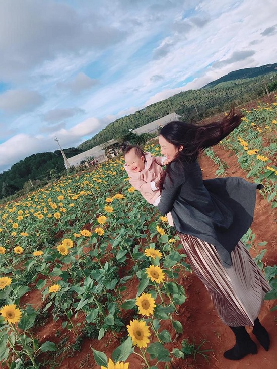 Con gái Phan Như Thảo toét miệng cười khi được mẹ bế đi ngắm cánh đồng hoa hướng dương.
