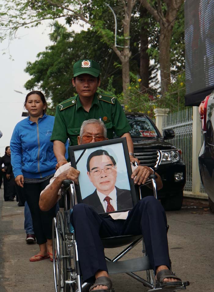 Một người dân cầm di ảnh nguyên Thủ tướng Phan Văn Khải, di chuyển trên xe lăn tới lễ an táng 